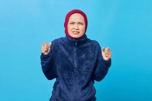 Angry young Asian woman screaming out with raised hand isolated on blue background photo