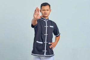 Portrait of Asian young man wearing taekwondo kimono doing stop motion with palm isolated on gray background photo