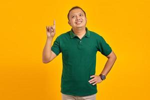 Sonriente joven asiático apuntando con el dedo hacia arriba y tener una idea sobre fondo amarillo foto
