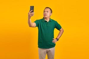 Portrait of confused asian young man using mobile phone when not connected to internet network over yellow background photo