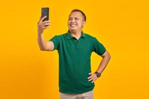 Cheerful young Asian man taking a selfie with a mobile phone on yellow background photo