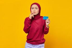 Beautiful Asian woman looking stressed and nervous with biting nails and showing credit card over yellow background photo