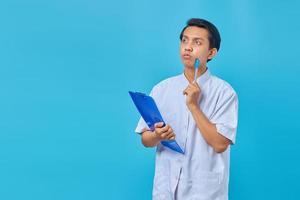 Handsome young male nurse concentrating thinking of ideas over blue background photo