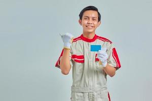 Portrait of handsome young mechanic showing credit card and pointing with finger at empty space with smiling expression on gray background photo