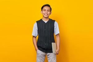 Portrait of cheerful Asian man carrying laptop over yellow background photo