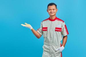 Portrait of smilling young Asian mechanic showing copy space in palms over blue background photo