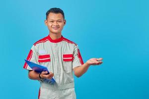 Portrait of excited young mechanic holding clipboard and pointing with palms pointing sideways isolated on blue background photo