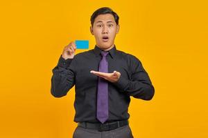 Surprised asian businessman showing credit card over yellow background photo