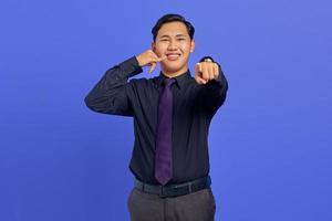 Portrait of attractive Asian man make call gesture sign and pointing at camera over purple background photo