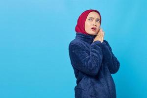 Shocked young Asian woman rub hands and looking aside on blue background