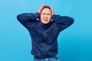 Retrato de mujer asiática joven enojada tapándose los oídos con la mano sobre fondo azul. foto