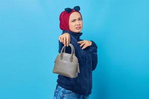 Beautiful young Asian woman holding bag with disgust and dislike expression on blue background