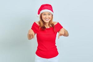 Portrait of young Asian woman wearing christmas dress smiling looking at camera and pointing finger down photo
