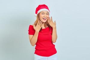 Portrait of cheerful young Asian woman in christmas hat raising hands over white background photo