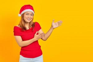 Cheerful young woman wearing a Christmas hat and extending her hand to the side inviting to come