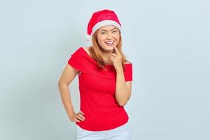 Photo of cheerful girl with christmas hat touching chin over white background