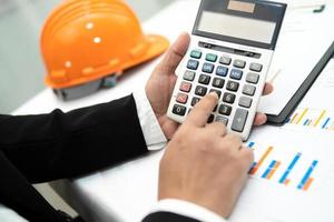 Engineer working project accounting with graph and construction helmet in office, Construction account concept. photo