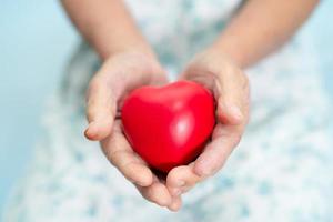 Paciente asiático mayor o anciano mujer sosteniendo un corazón rojo en su mano en la cama en la sala del hospital de enfermería, concepto médico fuerte y saludable foto