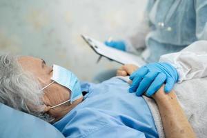 Doctor wearing  PPE suit new normal to check Asian senior or elderly old lady woman patient wearing a face mask in hospital for protect infection Covid-19 Coronavirus. photo