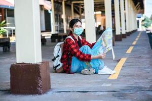 Female tourists sit and look at the map on the footpath beside the railroad. photo