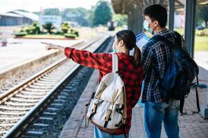 Male and female tourists look at the map beside the railway tracks. photo