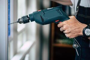 The carpenter holds the drill and drills the window. photo