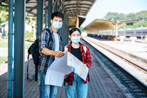 turistas masculinos y femeninos miran el mapa al lado de las vías del tren. foto