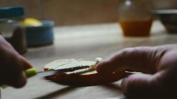 boter met een mes verspreiden op een vers sneetje tarwebrood, close-up van een hand die een mes vasthoudt, de zon schijnt. video