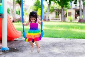 Adorable kid girl playing swing on playgrounds. Baby child wearing colorful dresses.