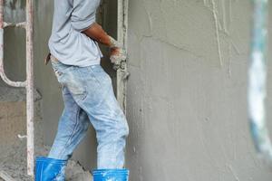 El enfoque selectivo en la superficie de la pared de cemento con manos borrosas del trabajador enyesado del cemento en segundo plano. foto