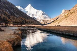 Sacred snow mountain Yangmaiyong reflection on river in autumn valley on plateau