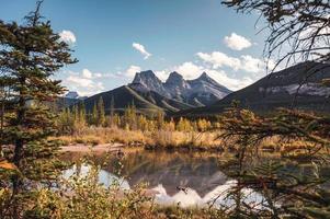 Tres hermanas montañas en el bosque de otoño reflexión sobre el estanque en Canmore, Canadá foto