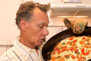 Hombre maduro en su cocina admirando su pizza margarita casera foto