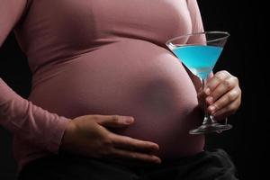 Close up pregnant woman holding blue cocktail in glass on black background photo