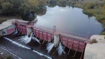 il volo lento di un drone aereo su una diga fluviale da cui sgorga l'acqua nella campagna. video