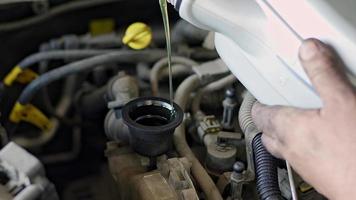 Maestro de reparación de automóviles vertiendo aceite nuevo en el metraje del motor