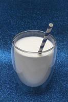 Festive concept. On a shiny blue background, a glass of milk with a straw. Vertical photo.