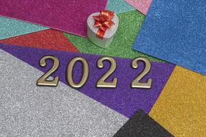 On a colorful bright shiny New Year background, a silver gift box with a red bow and golden numbers 2022. Concept for New Year's card. photo