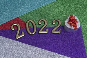 On a colorful bright shiny New Year background, a silver gift box with a red bow and golden numbers 2022. Concept for New Year's card photo