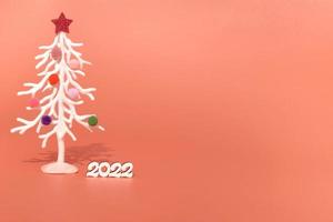 tarjeta de Navidad. con el telón de fondo de las luces de Navidad, un árbol de Navidad blanco en juguetes de piel multicolor con los números 2022. espacio de copia foto