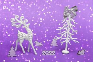 Merry Christmas and Happy New Year. Festive poster with a Christmas tree, a deer, a sleigh on a purple background with lights. New year 2022 copy space close up photo
