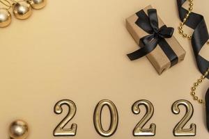 año nuevo 2022. vista superior maqueta de año nuevo sobre fondo beige cinta negra, caja de regalo, números dorados y destellos multicolores. diseño de postales foto