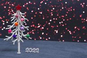 Christmas card. Against the background of Christmas lights, a white Christmas tree in multi-colored fur toys with the numbers 2022. copy space photo