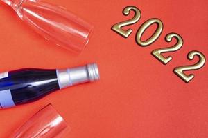 Top view flat new year mockup on red background with numbers, champagne and glasses. Close-up. New Year 2022, with copy space photo