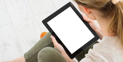 Chica adolescente con un tablet pc sentado en el suelo de una sala de estar, tocando la pantalla en blanco foto