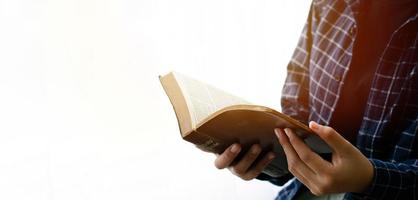 Leer el primer plano de la Biblia de la mano de una mujer leyendo la Biblia junto a la ventana fondo blanco.