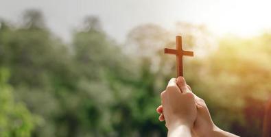 Chica sosteniendo una cruz para orar gracias a Dios alabar al señor con el fondo al aire libre, orar, la pascua y el concepto de buenas vacaciones foto