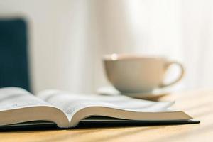 Biblia abierta con una taza de café blanco con el ambiente de la mañana en una mesa de madera cerca del alféizar de la ventana foto