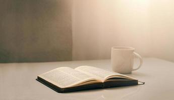 abra una biblia junto a la ventana con una taza de café para la luz de la mañana. y ponerlo sobre una mesa de madera con luz de ventana foto