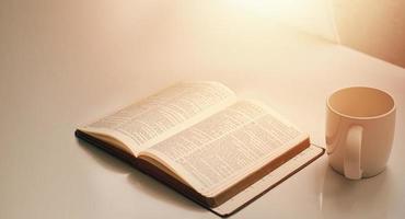 Open a bible by the window with a cup of coffee for the morning light. and put it on a wooden table with a window light photo